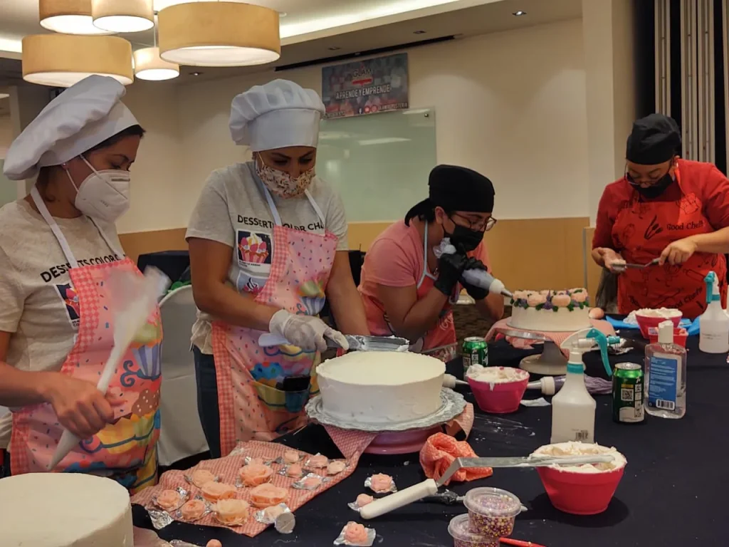 Estudiantes con cofia y delantal aplican betún blanco y flores de azúcar durante un curso de repostería CDMX presencial.