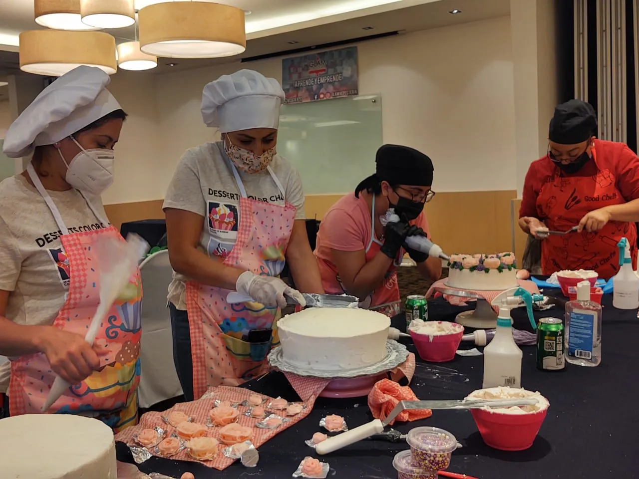 Estudiantes con cofia y delantal aplican betún blanco y flores de azúcar durante un curso de repostería CDMX presencial.