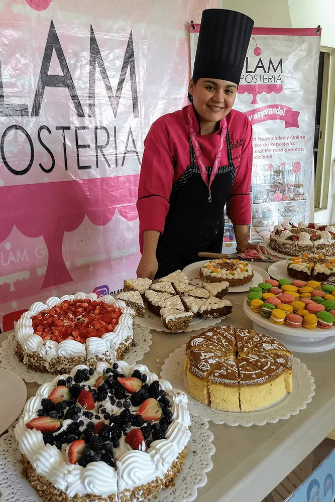 Una chef sonriente presenta diversos pasteles de frutas, macarons y pays durante un curso de repostería profesional.