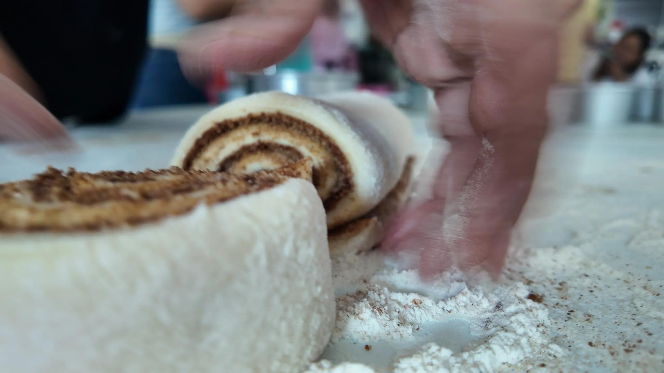 Primer plano con desenfoque de movimiento de unas manos enharinando la superficie para trabajar la masa de rollos de canela en un curso presencial.