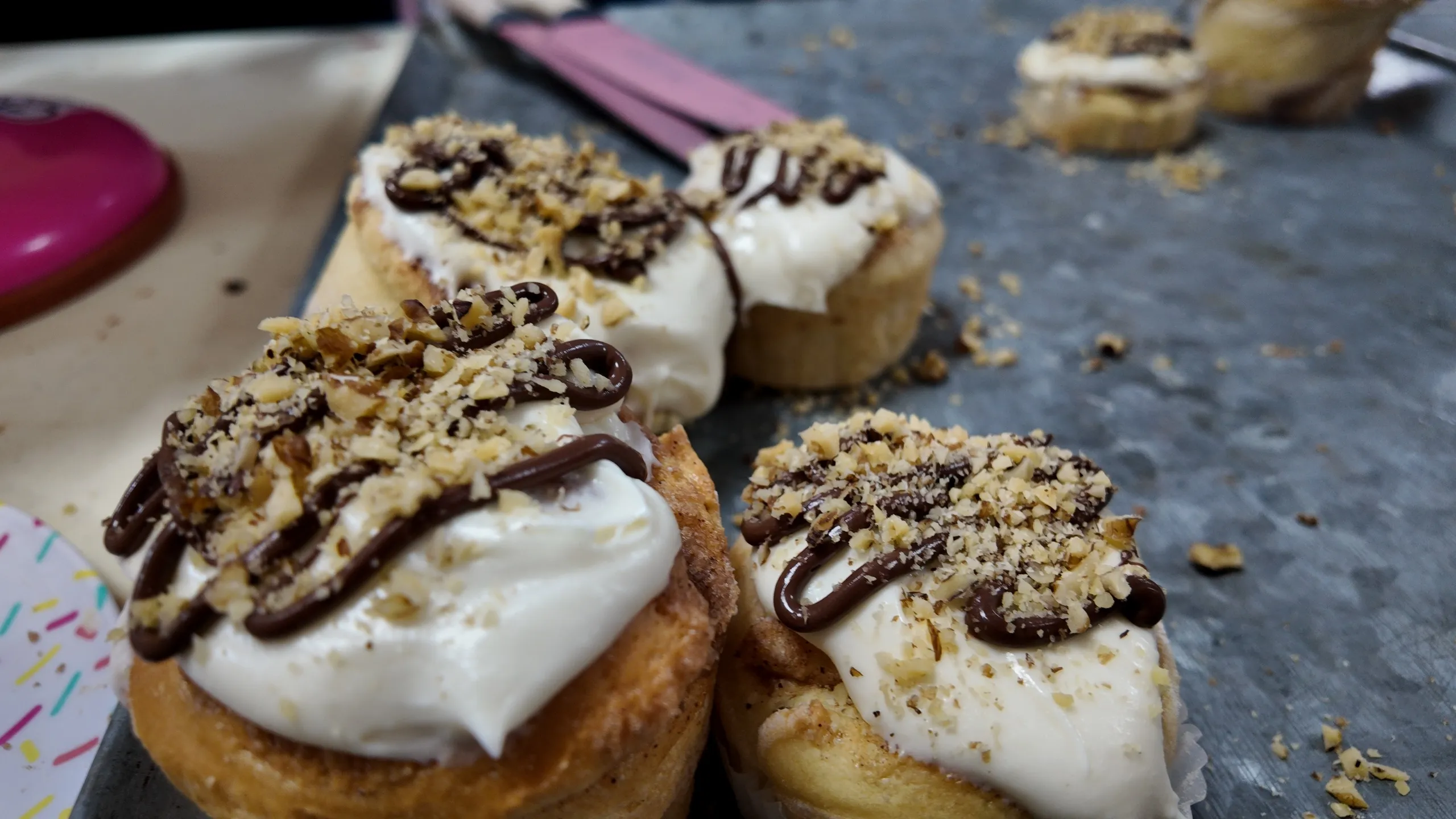 Una vista de arriba hacia abajo de una fila de rollos de canela horneados y glaseados con chocolate y nueces picadas en primer plano.