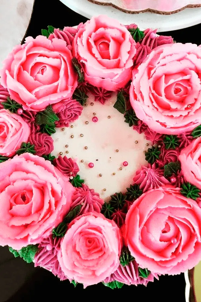Acercamiento a un pastel decorado con flores de crema de mantequilla rosa y perlas comestibles en curso de repostería técnica.