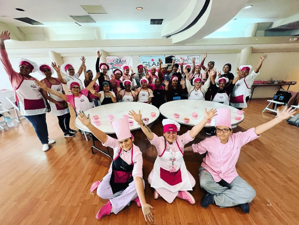 Vista aérea de alumnos y maestros uniformados celebrando efusivamente con diplomas y pasteles al concluir el curso de repostería integral.