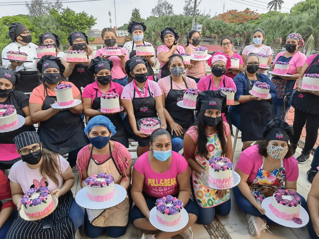 Decenas de reposteras posan orgullosas en el exterior con sus pasteles terminados decorados en tonos lavanda en el curso de repostería.