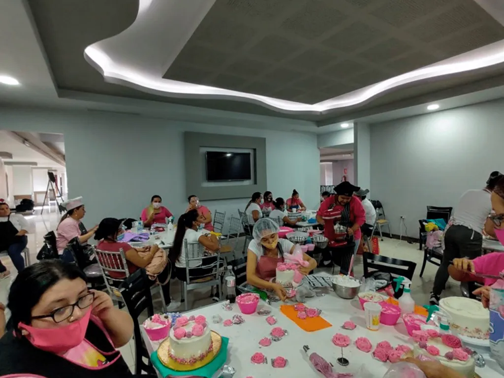 Equipo completo de la academia posa celebrando alrededor de una mesa repleta de mini pasteles de boda en el curso de repostería avanzada.