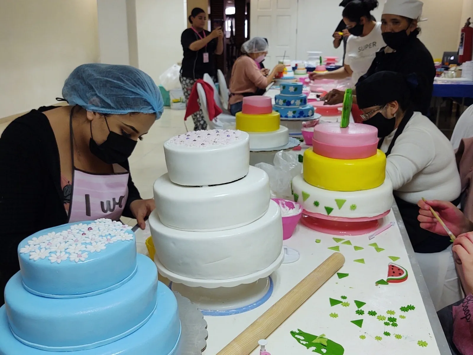 Grupo de mujeres emprendedoras aprendiendo técnicas de decoración de pasteles con fondant y flores en un curso práctico.