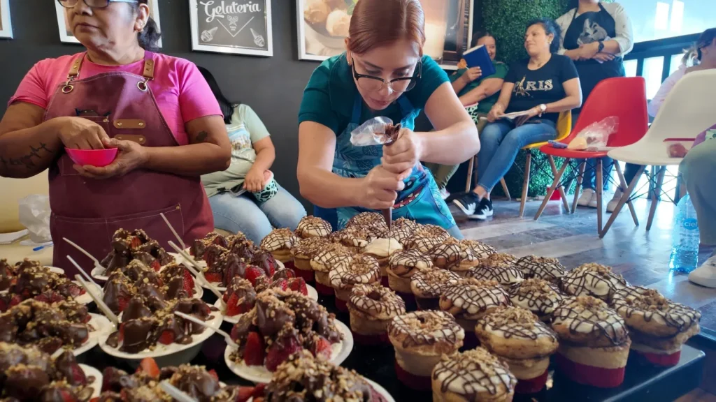 Mujeres emprendedoras decorando postres con chocolate y fresas en un taller de repostería creativa y capacitación.