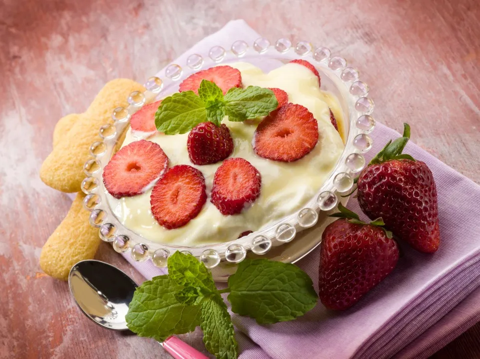 Postre cremoso tipo carlota de limón en tazón de vidrio, decorado con fresas fileteadas y hojas verdes de menta.