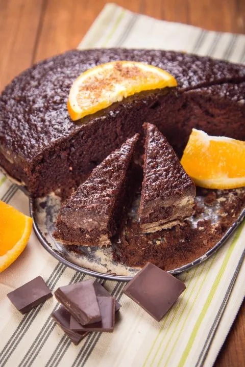 Porción de pastel de chocolate con cobertura brillante de fudge sobre una servilleta azul junto a un tenedor.